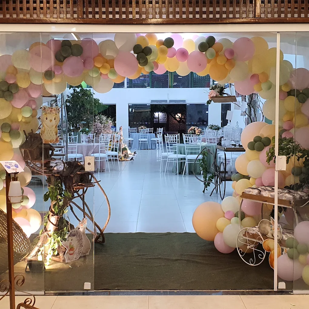Entrada do espaço decorada com um grande arco de balões pastel, com mesas e cadeias brancas ao fundo