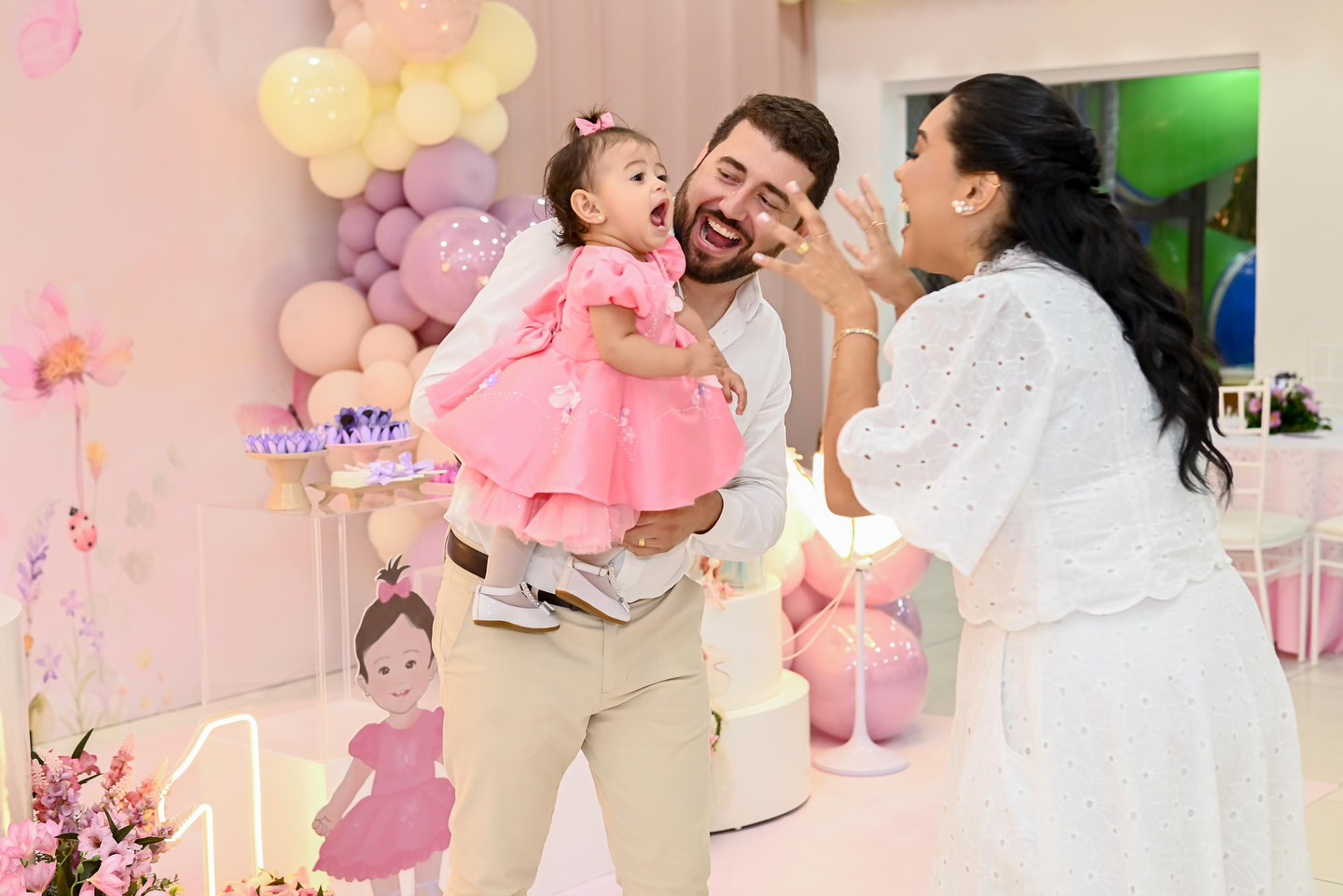 Família comemorando o primeiro aniversário de uma menina em meio a balões pastel, no salão da Hari Raya Eventos